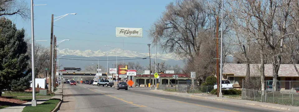 Denver Avenue in Fort Lupton looking west, a Fort Lupton banner over the road and the snow-covered Front Range beyond the rooftops
